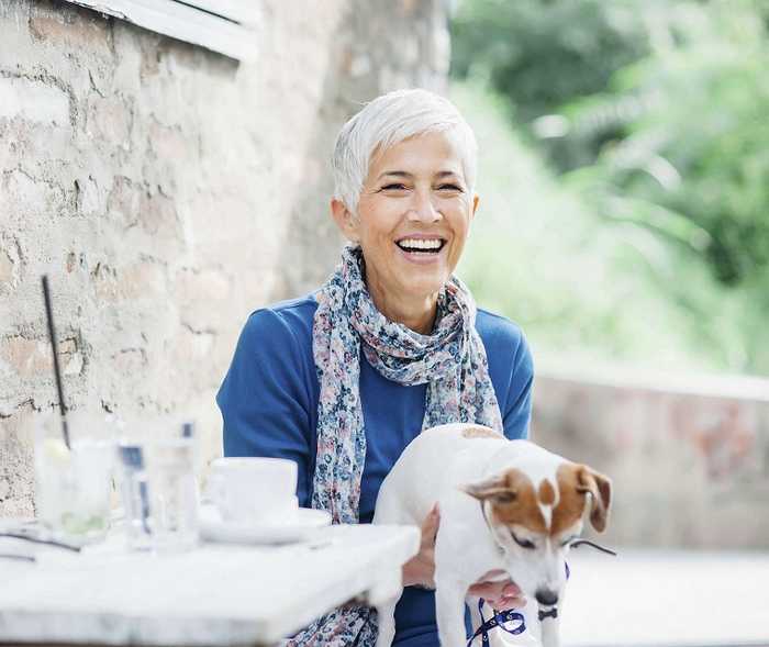 Ältere Frau lacht mit Hund auf dem Schoß