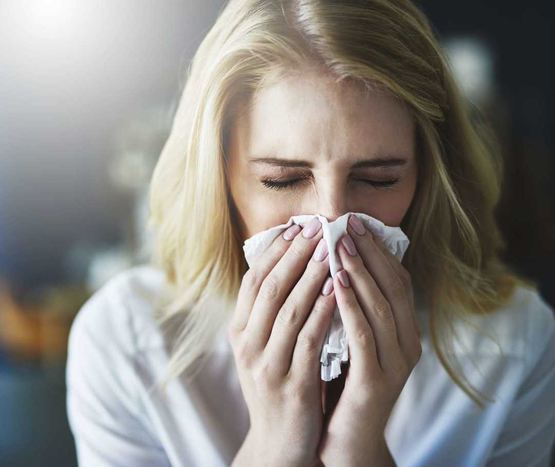 Junge Frau putzt sich die Nase mit einem Taschentuch