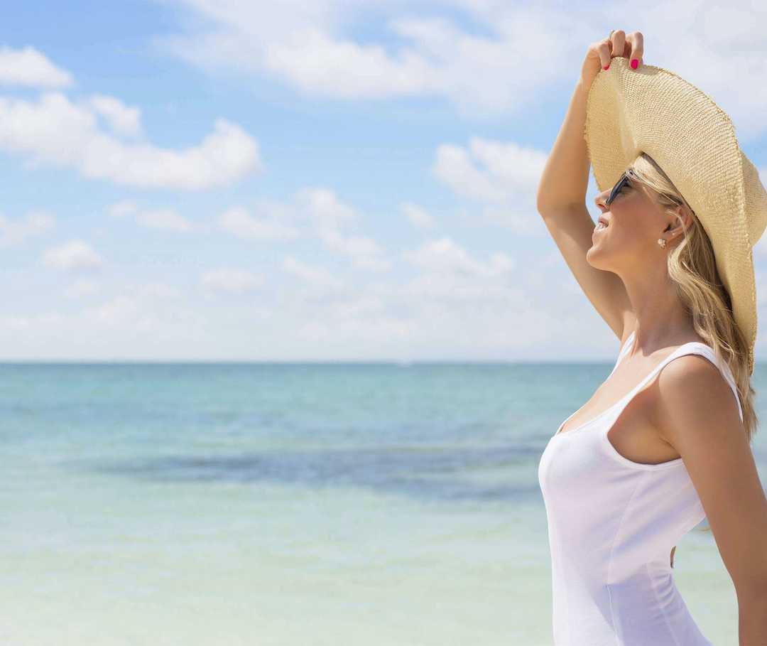 Junge Frau mit Sonnenhut schaut aufs Meer