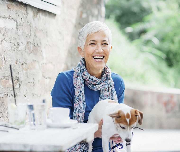 Ältere Frau lacht mit Hund auf dem Schoß